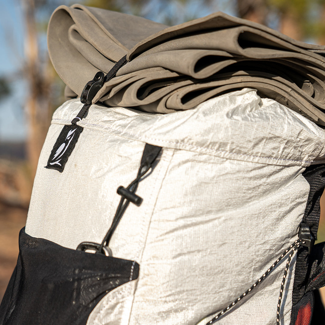 Close-up shot of the Outdoor Vitals CS40 Ultra Backpack showing a foam sleeping pad secured to the top lid using the integrated Y-strap compression system.