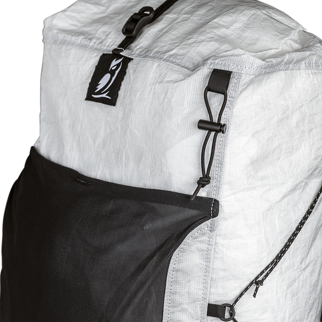Close-up view of the upper front panel of the Outdoor Vitals CS40 Ultra Backpack, showing the owl logo tab, roll-top compression strap buckle, front mesh pocket, and side cord attachment points.