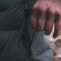 Close-up of a person's hand unzipping the side pocket of a dark gray puffer jacket.