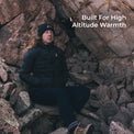 woman sits in rocky area wearing a black puffy down jacket.