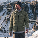 A man wearing a green insulated puffer jacket stands in a snowy mountain landscape. White text labels point to the jacket, reading 'YKK Zippers' near the chest zipper area and 'Insulated Pockets' near the lower pocket area.